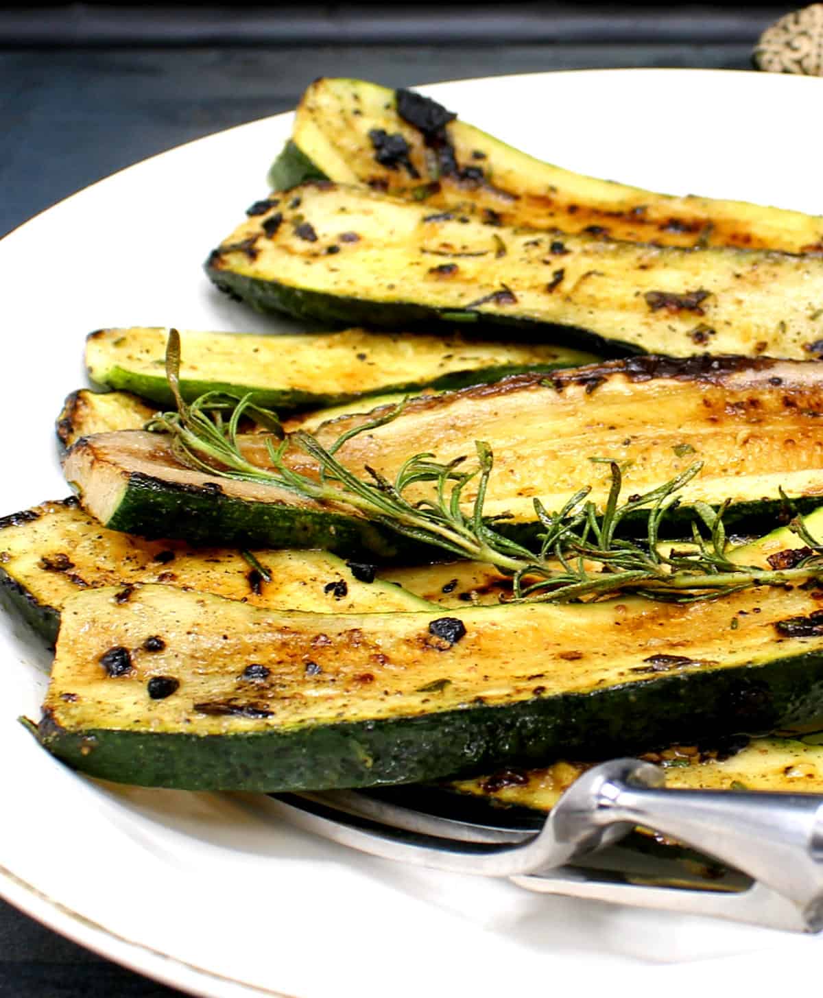 Closeup image of slices of pan roasted zucchini with a rosemary sprig.