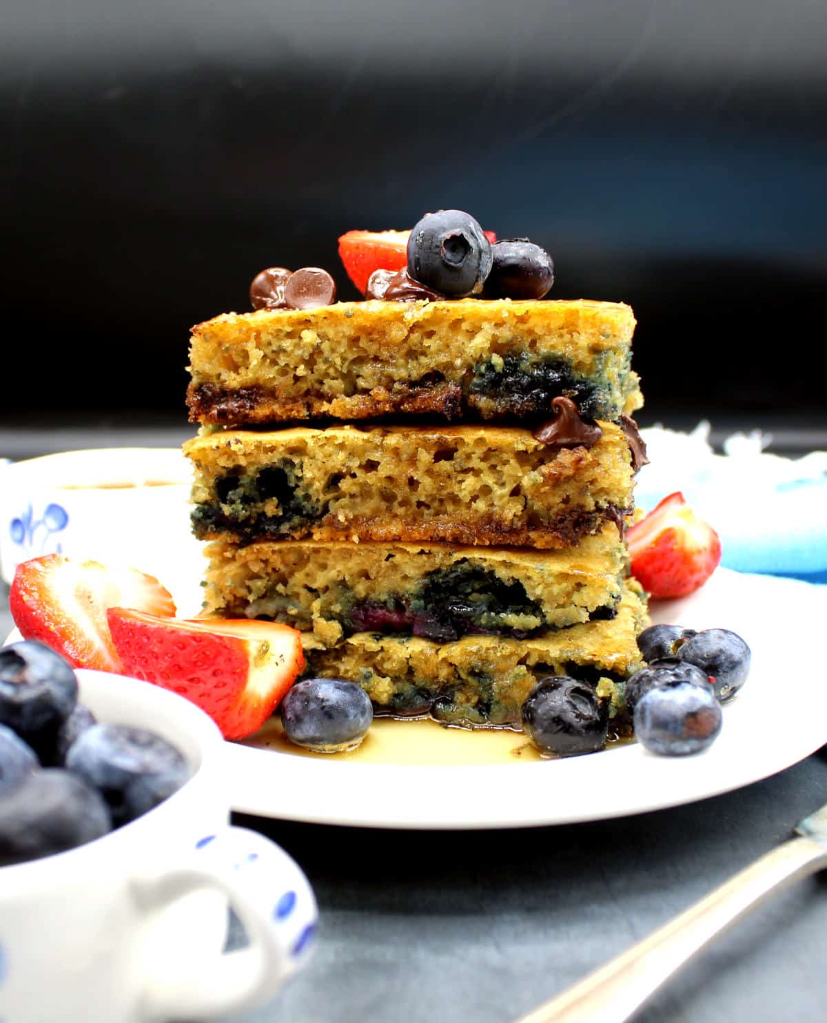 Photo of a stack of four vegan sheet pan pancakes with fresh berries and maple syrup.