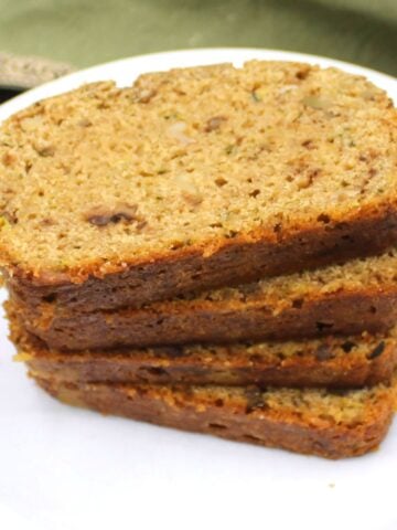 Slices of vegan zucchini bread stacked on white plate.