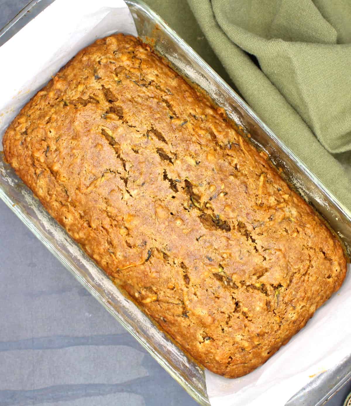 Vegan zucchini bread out of the oven in glass loaf pan lined with parchment paper.