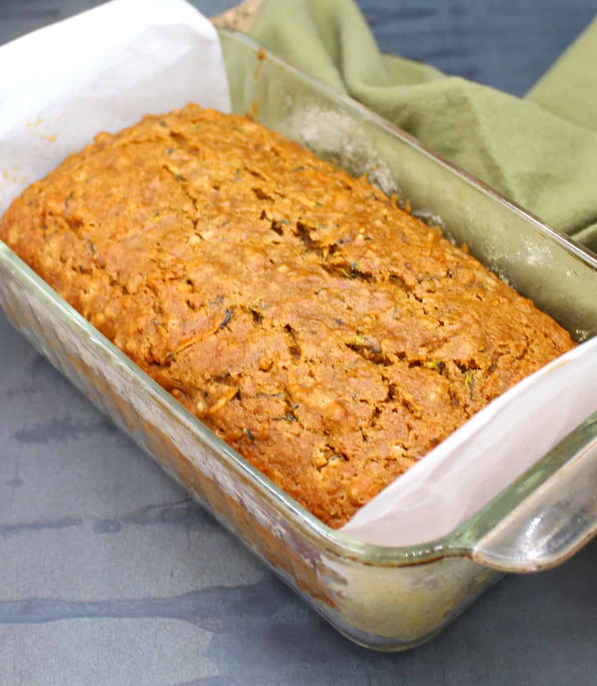 Loaf of zucchini bread in glass pan lined with parchment paper.