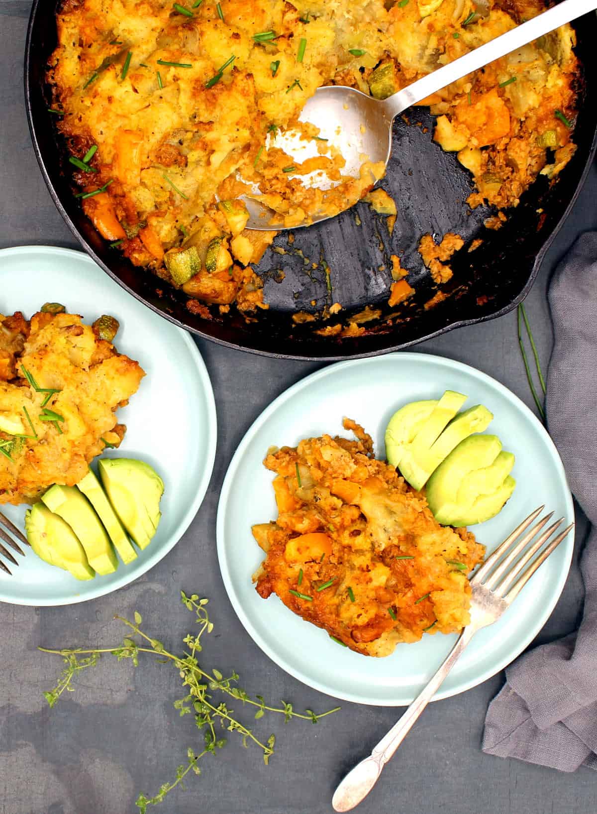 Cheesy vegan dinner bake in skillet and served in two blue-green plates with avocado.