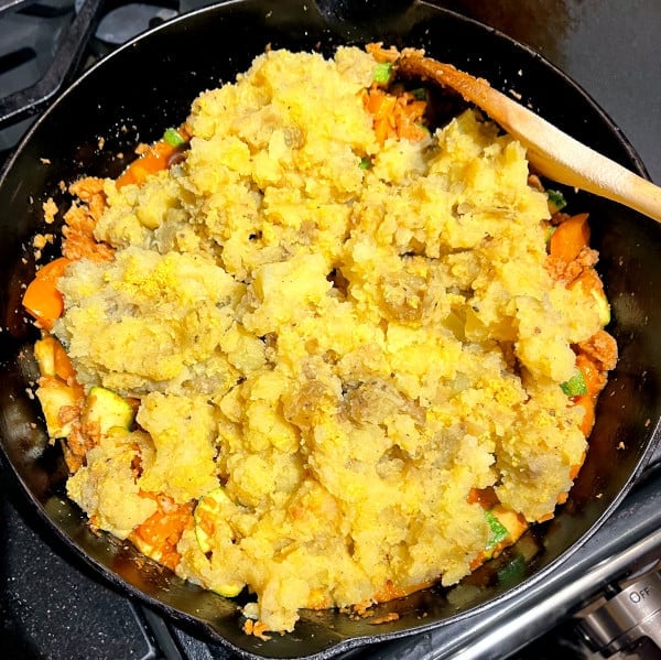 Cheesy vegan dinner bake with cheesy mashed potato topping in cast iron pan
