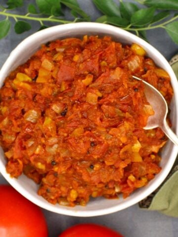 A bowl of tomato chutney with tomatoes and curry leaves around it.