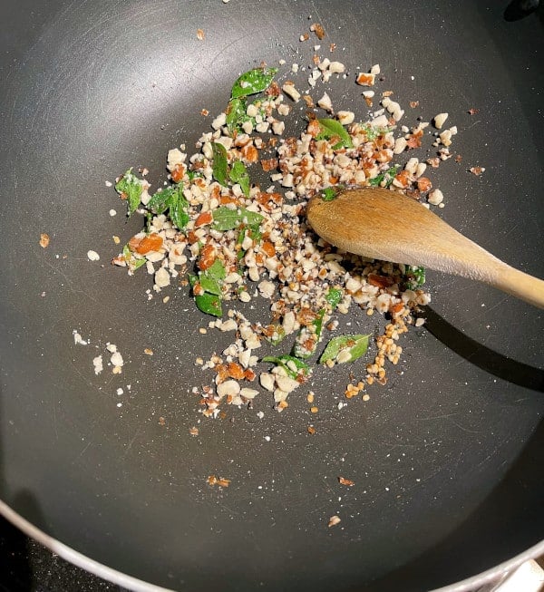 Curry leaves, peanuts, urad dal and mustard seeds in wok frying