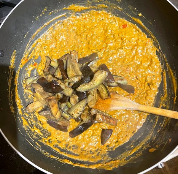 Roasted eggplants added to dahi baingan sauce in wok.