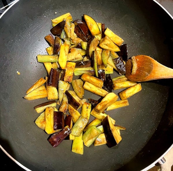 Browned eggplant slices in wok with wooden spoon.