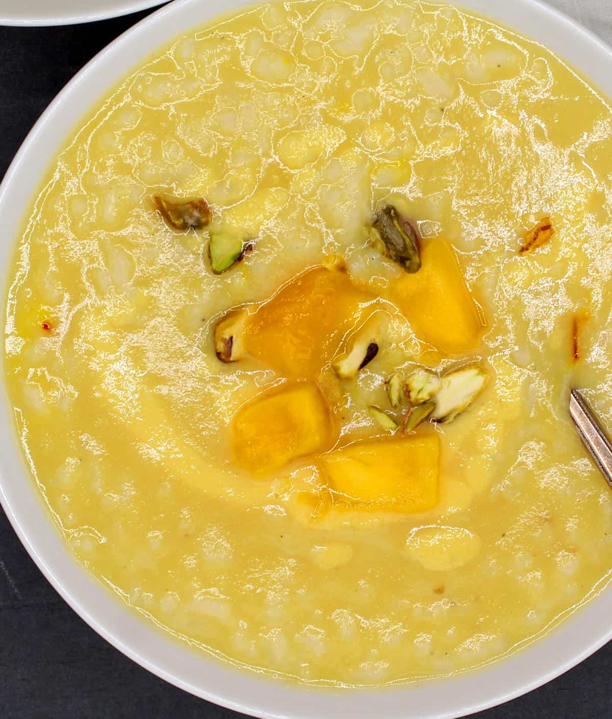Overhead closeup of a bowl of vegan mango coconut congee with a garnish of pistachios and mangoes.
