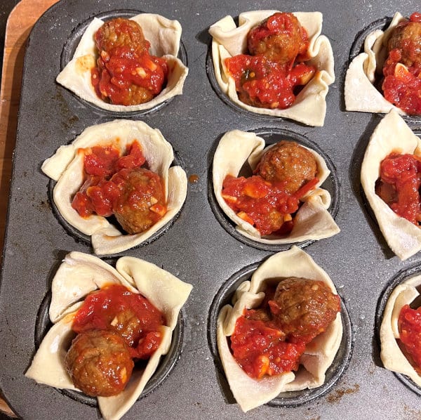 Puff pastry cups in muffin tins filled with vegan marinara meatballs.