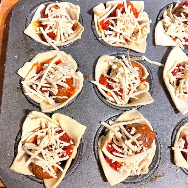 Unbaked puff pastry cups with marinara meatballs and vegan cheese shreds.