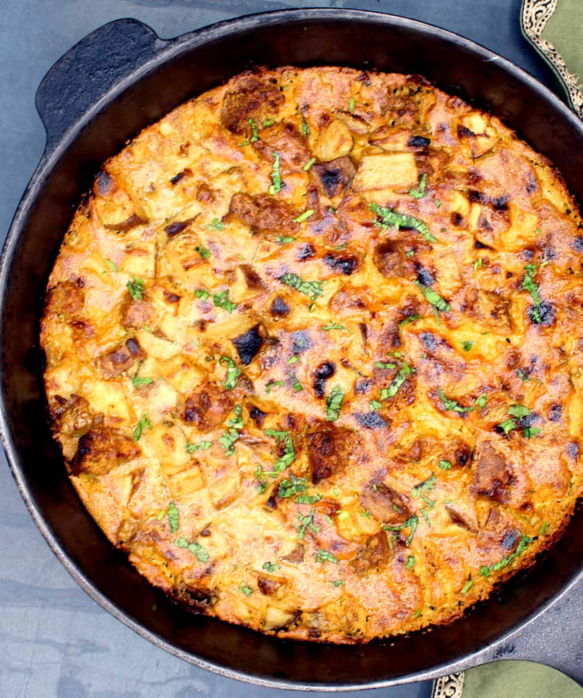 Vegan breakfast casserole with potatoes and vegan sausage and cheesy cashew cream, in black cast iron griddle.