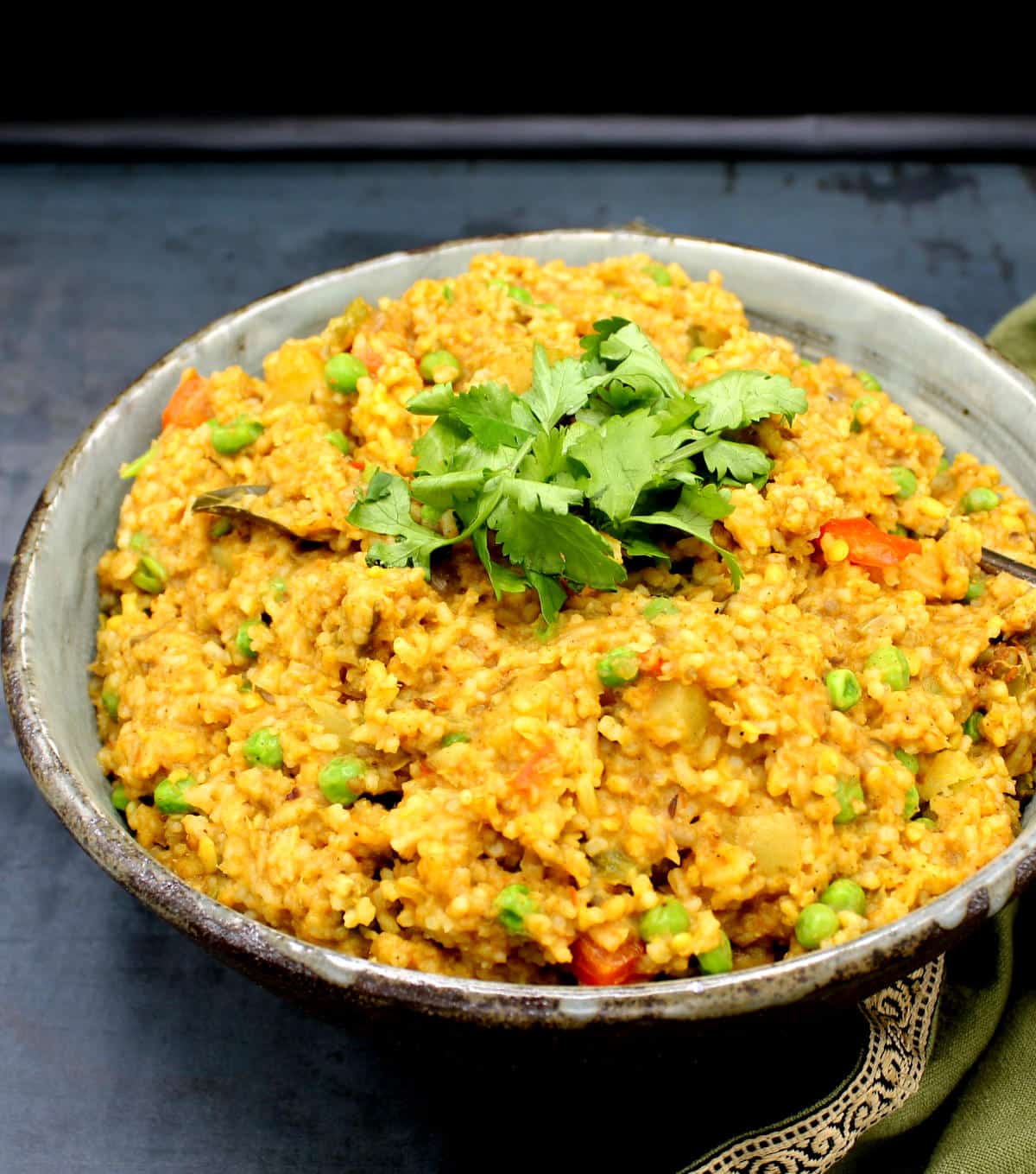Front photo of a large earthenware bowl filled with masala khichdi, an Indian rice and lentil dish, with cilantro garnish.