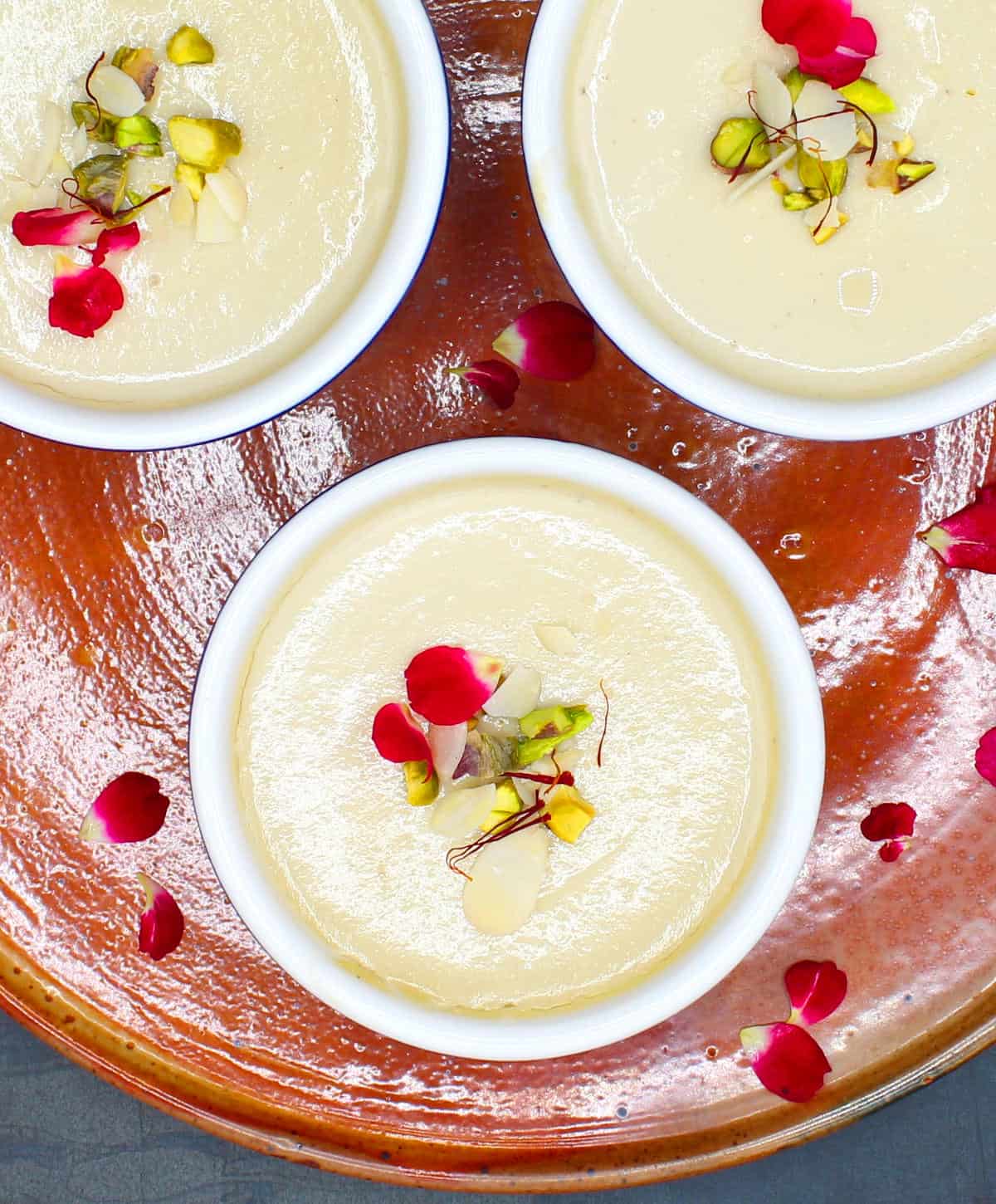 Overhead photo of ramekins with vegan, dairy-free mishti doi with nuts and rose petals.