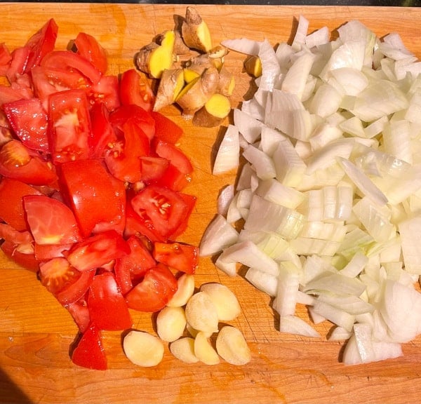 Tomatoes, garlic, onions and ginger on chopping board.