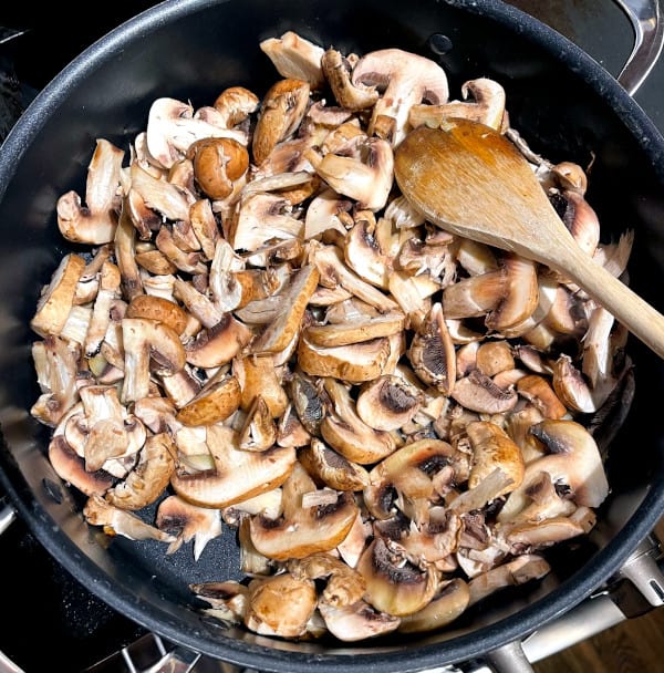 Sliced mushrooms in pot with a wooden spoon.