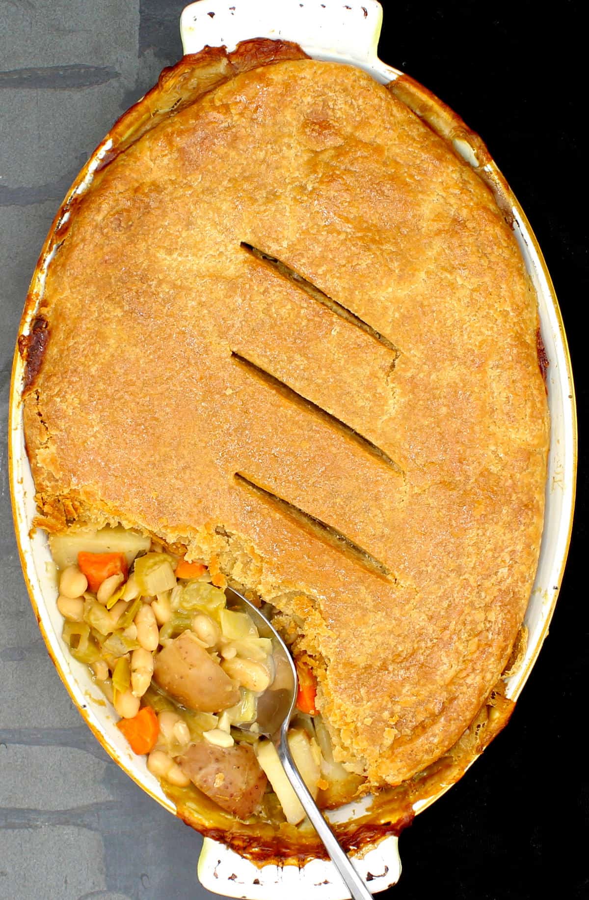 Overhead shot of a vegan pot pie with a golden whole wheat crust and a filling of beans and potatoes.