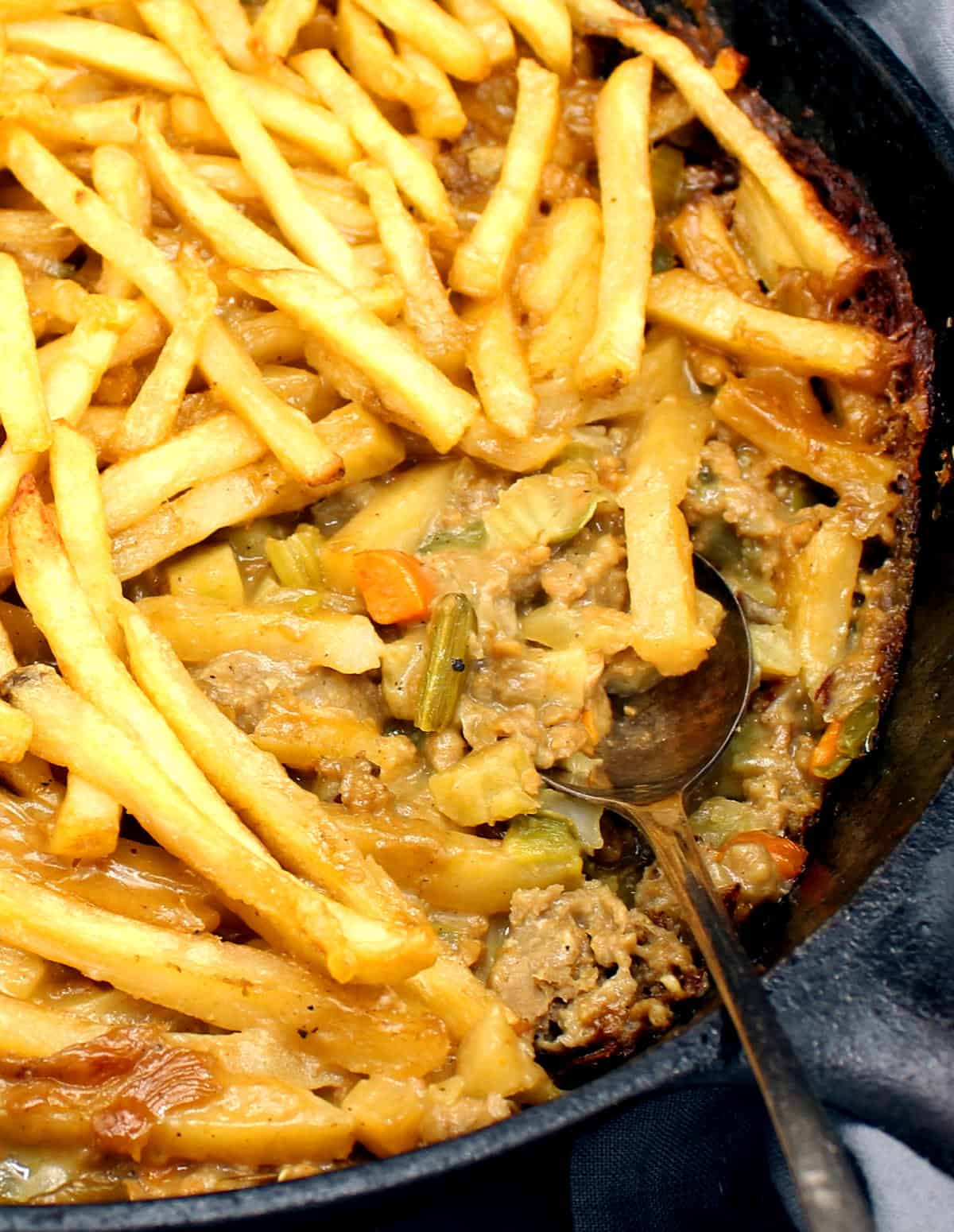 Closeup photo of vegan French Fry casserole with golden potato fries layered over vegan beef and veggie filling.