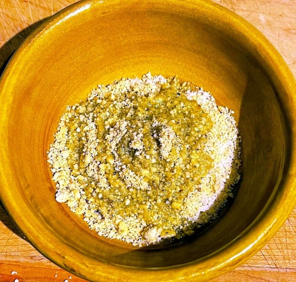 Breadcrumbs mixed with olive oil and vegan parmesan in bowl.