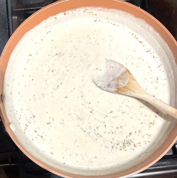 Creamy white sauce with herbs added in skillet.