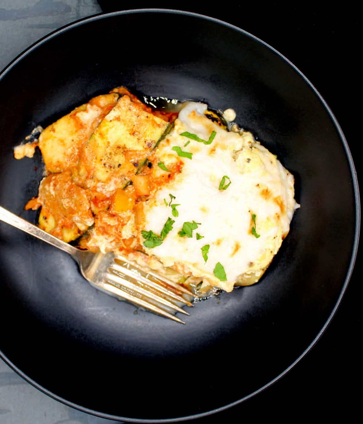 A serving of vegan zucchini lasagna in a black bowl with fork.