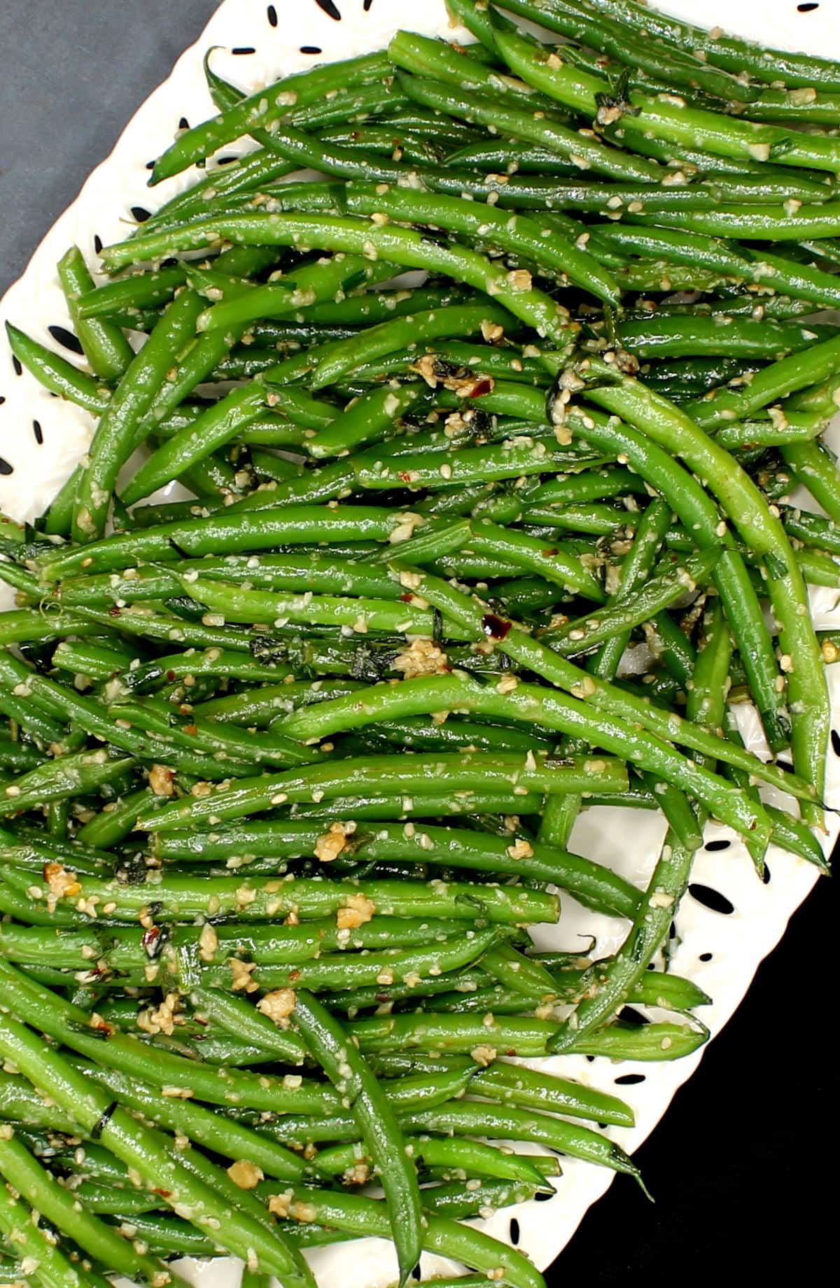 Overhead diagonal shot of green beans with garlic and sesame on a white platter.