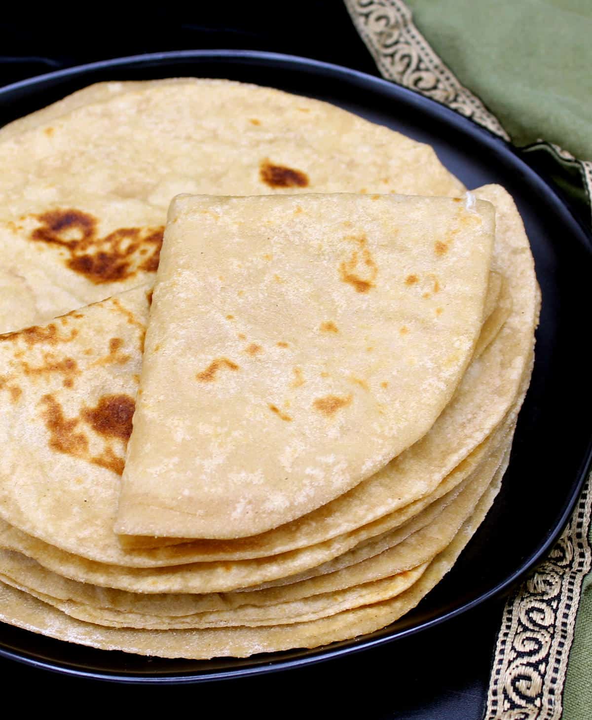 Front photo showing a roti folded over twice on a stack of rotis in black plate.