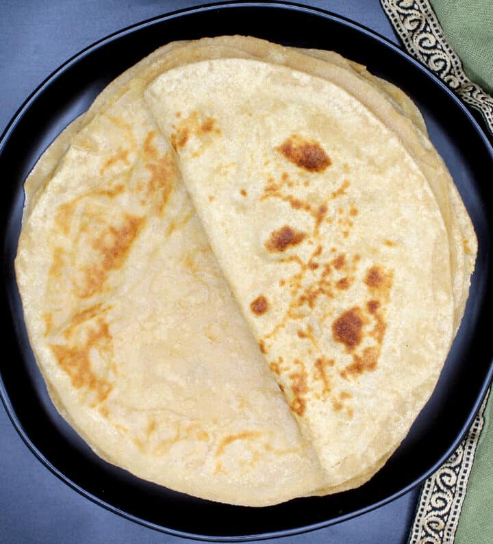 Overhead photo of a stack of soft rotis on a black plate with green napkin.