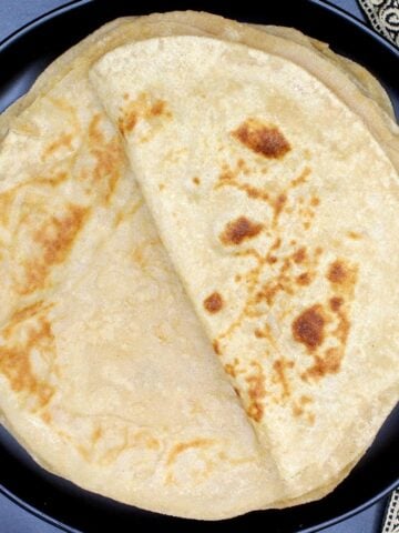 Soft rotis stacked on a black plate.