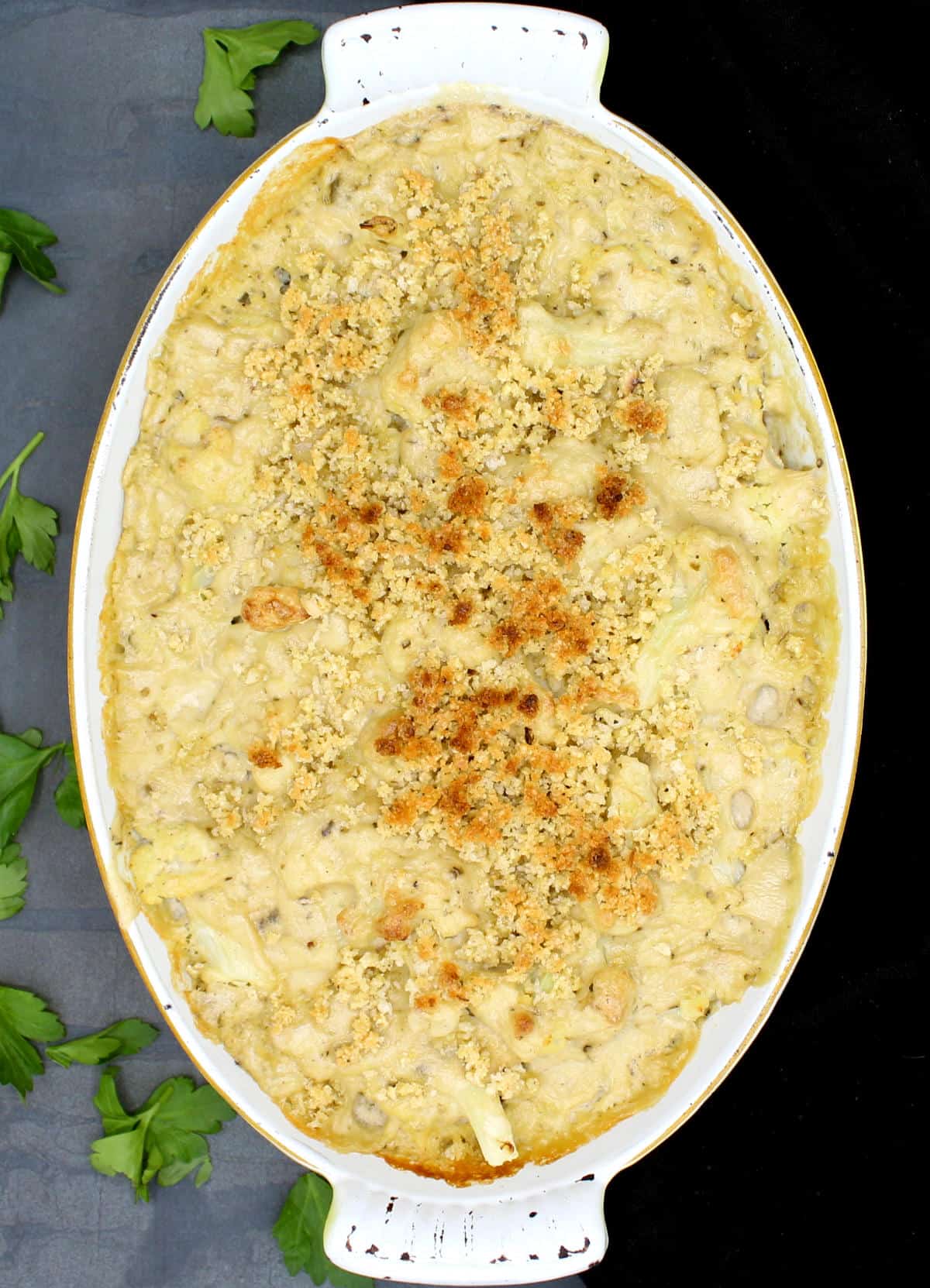 Overhead shot of creamy vegan cauliflower casserole in a baking dish surrounded by parsley leaves.
