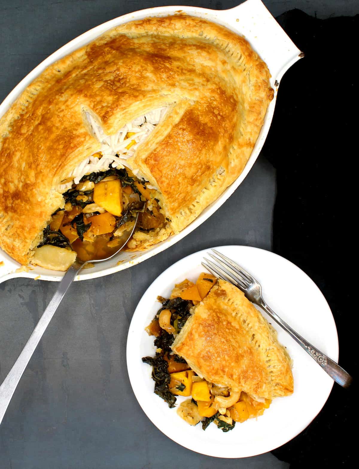 Vegan butternut squash and kale pie in baking dish with a portion on a white plate.