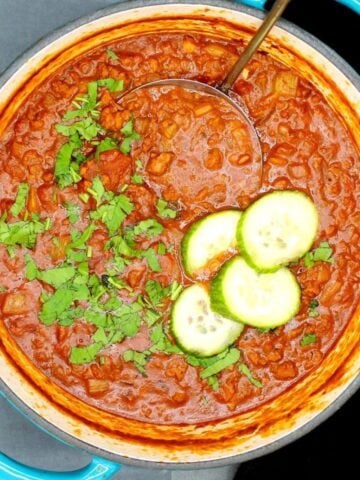 Low carb vegan keto chili in a blue dutch oven with cucumber and parsley.