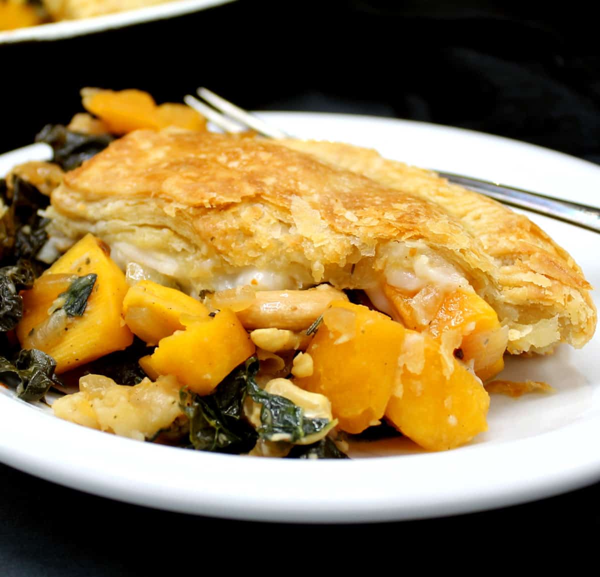 Closeup of a crispy, golden vegan sourdough pie crust with a savory filling of squash and greens.