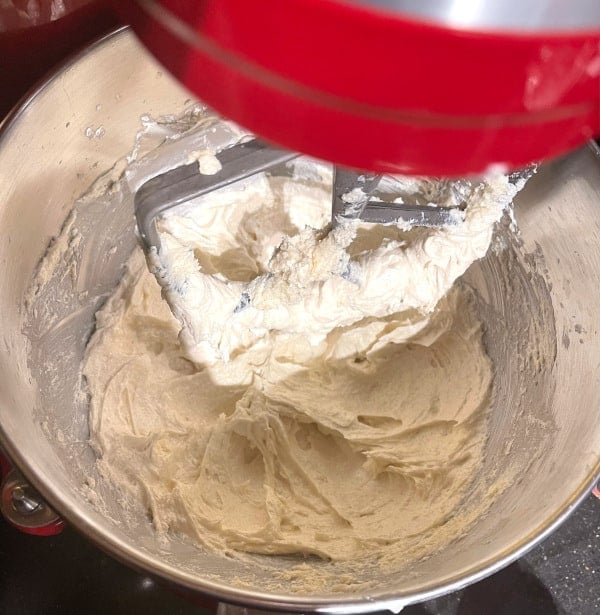 Butter and sugar mixed with aquafaba and vanilla and almond extracts in stand mixer bowl.