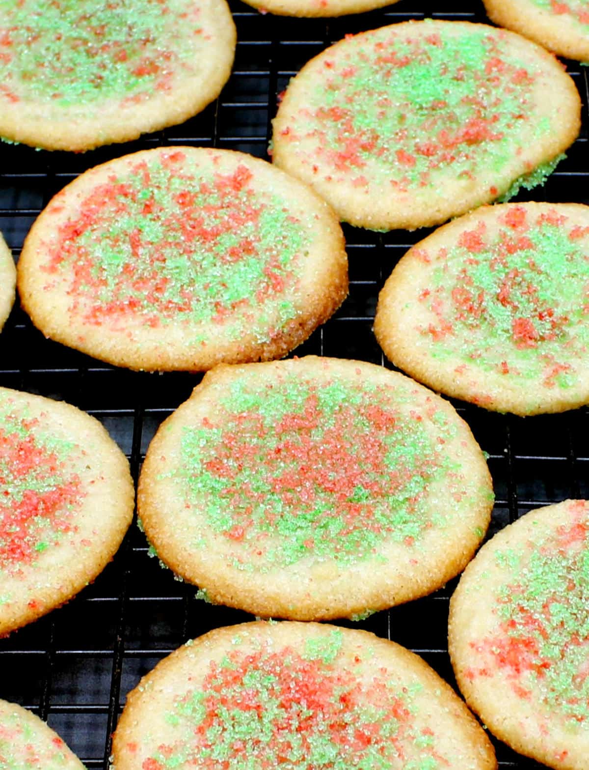 एक तार रैक पर रंगीन चीनी शीतलन के साथ सजाए गए शाकाहारी बादाम कुकीज़ की सामने की तस्वीर।