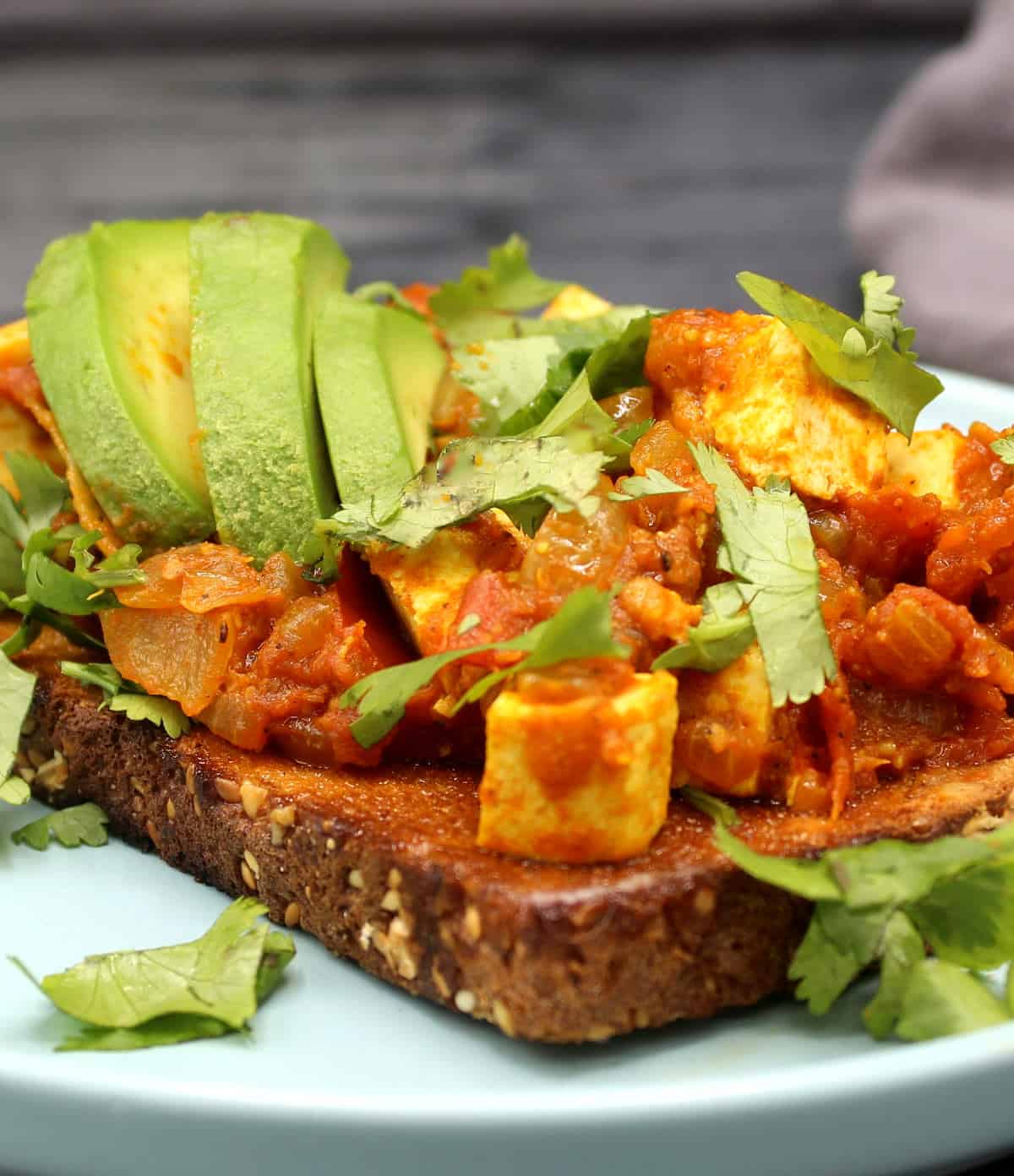 Closeup of tomatoes with tofu eggs served over a slice of wholegrain toast with slices of avocado.