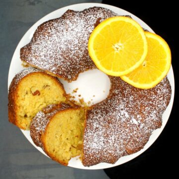 An overhead shot of a sliced vegan Greek new year's cake with two slices of oranges.