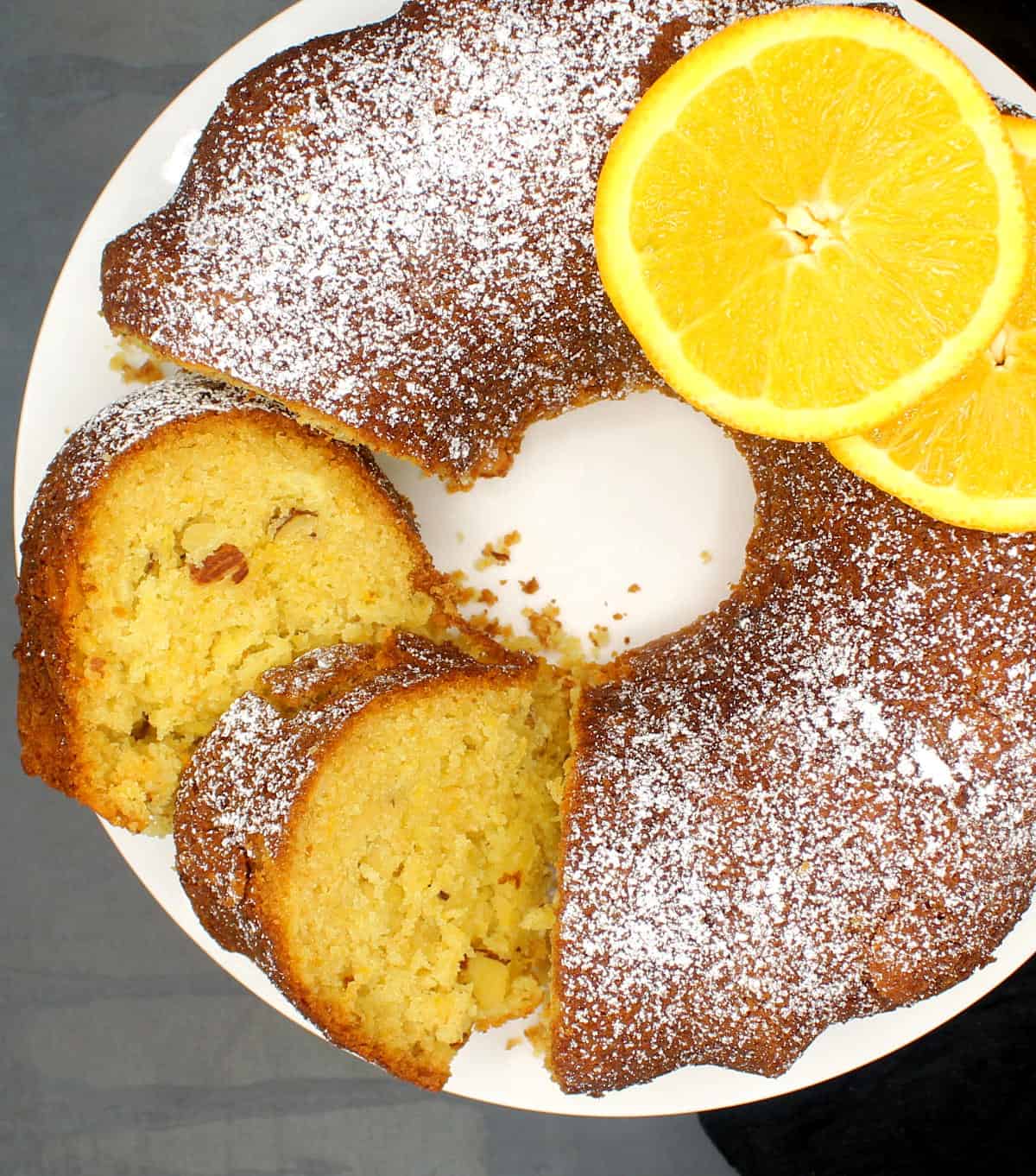 Overhead shot of a sliced Greek new year's cake with orange slices and a dusting of powdered sugar.