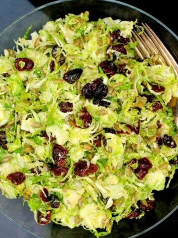 Overhead closeup of vegan brussels sprouts salad in glass bowl with cranberries, sunflower seeds and maple dijon dressing.