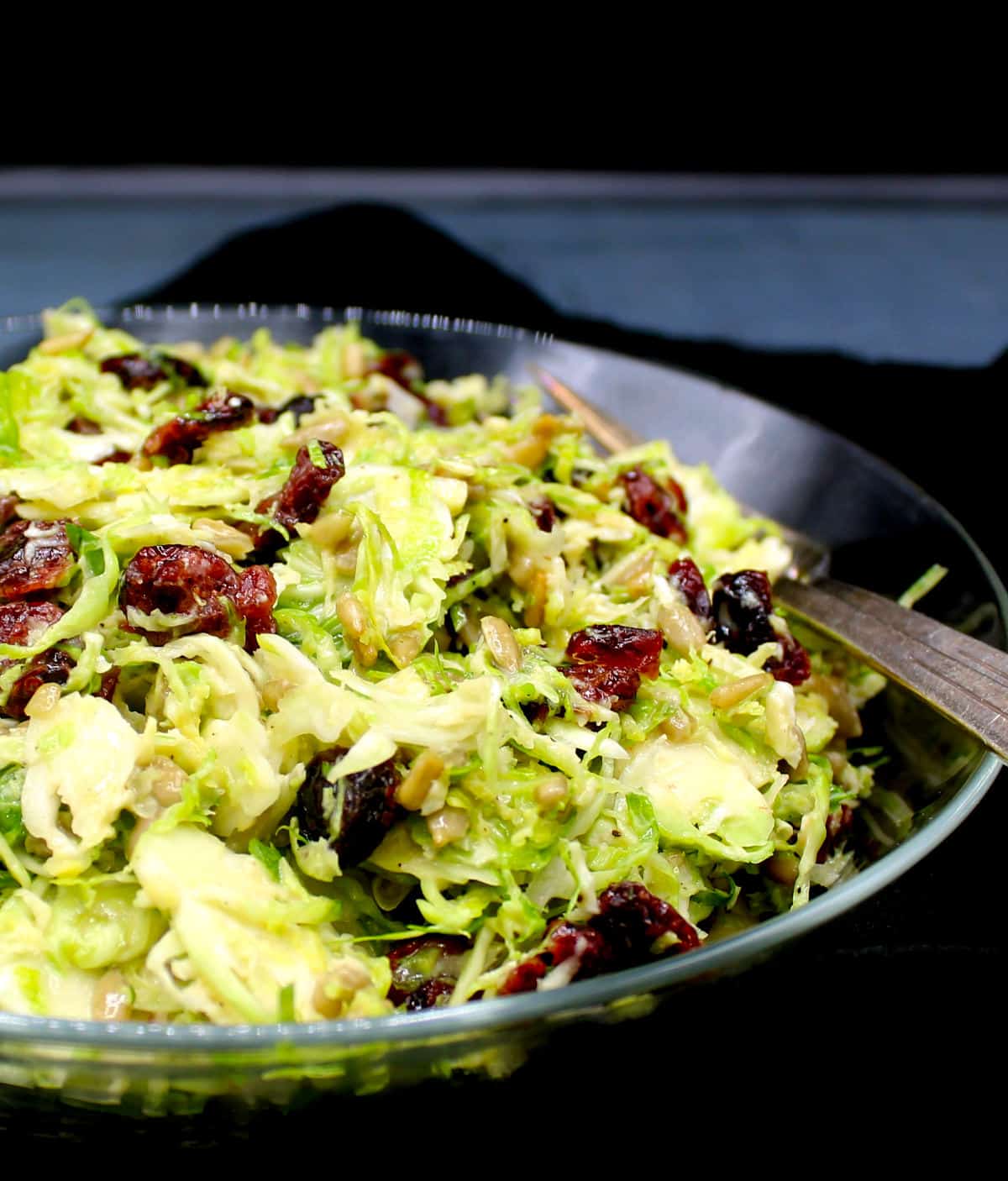 A front partial shot of vegan brussels sprouts salad in a glass bowl with forks.