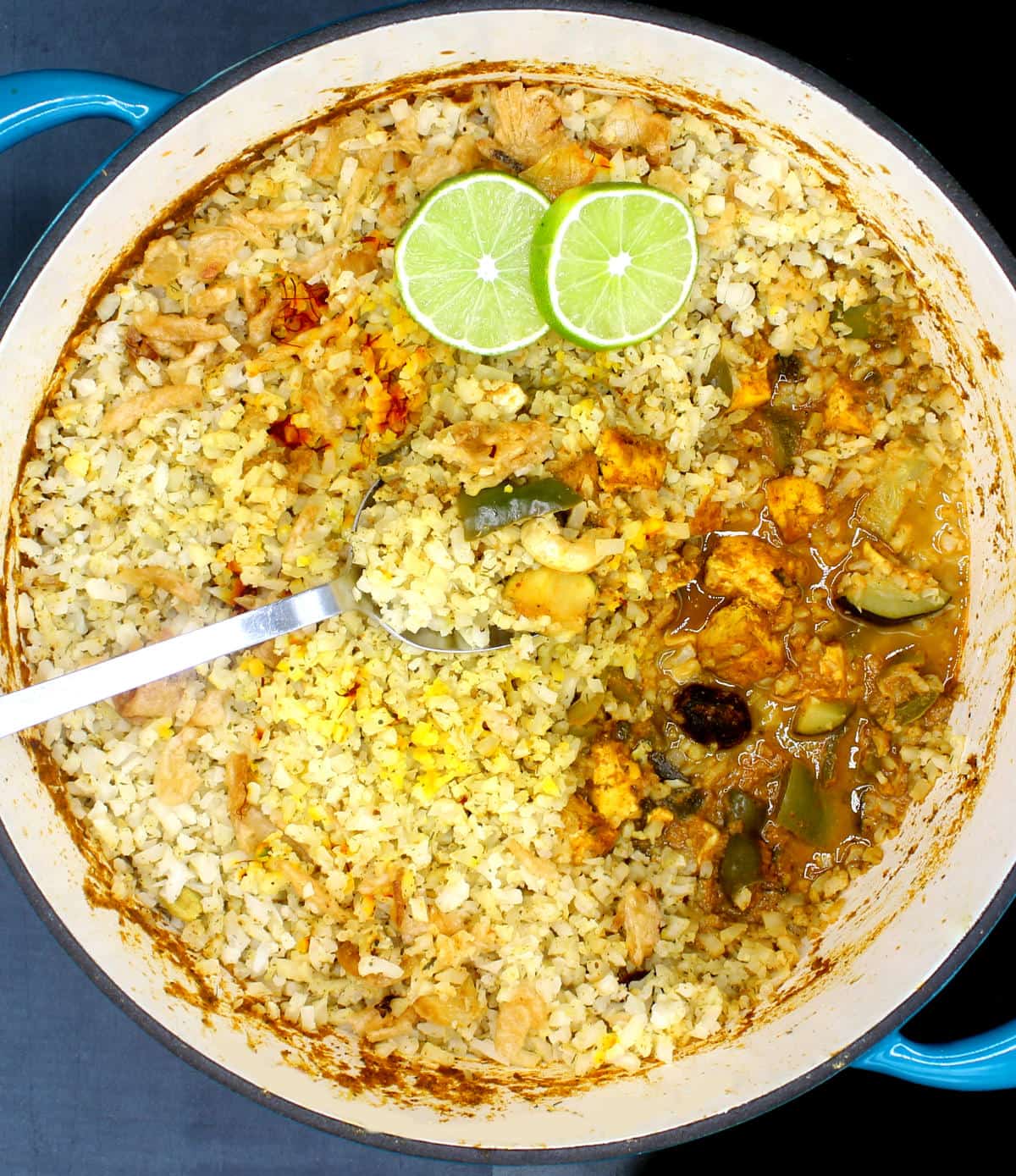 Cauliflower rice biryani in Dutch oven with slices of lime and a steel spoon.