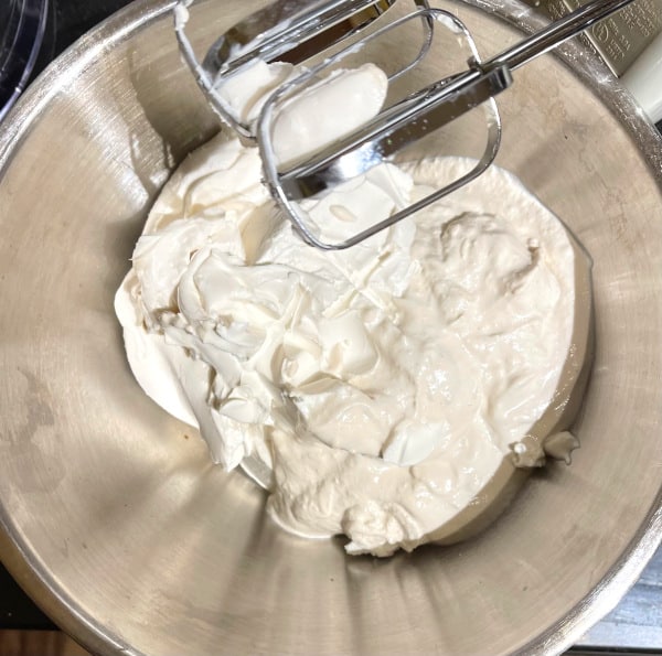 Yogurt and vegan cream cheese in bowl with stand mixer beaters showing.