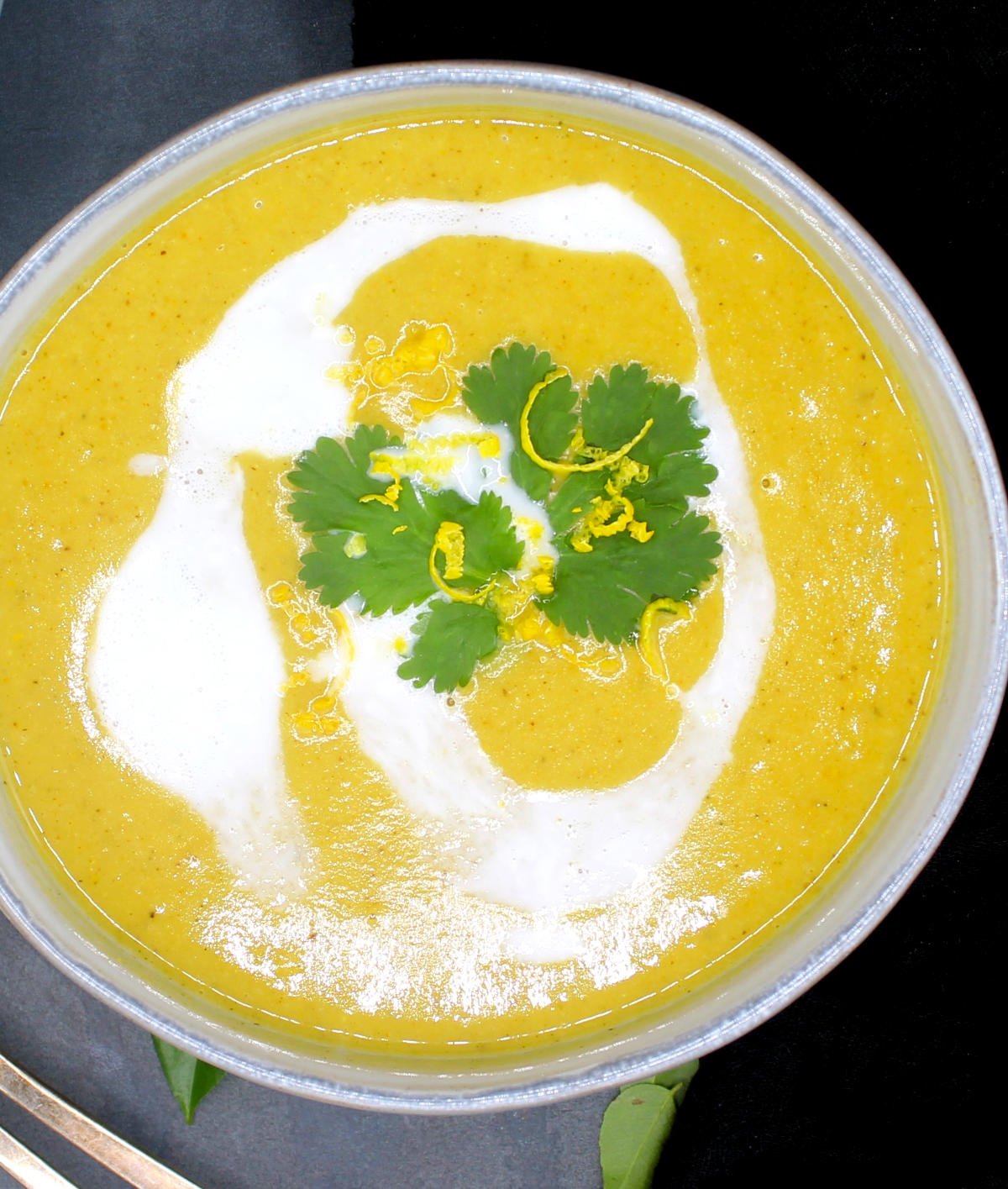 Overhead partial closeup photo of a bowl of mulligatawny soup with cilantro and lemon zest and coconut cream.