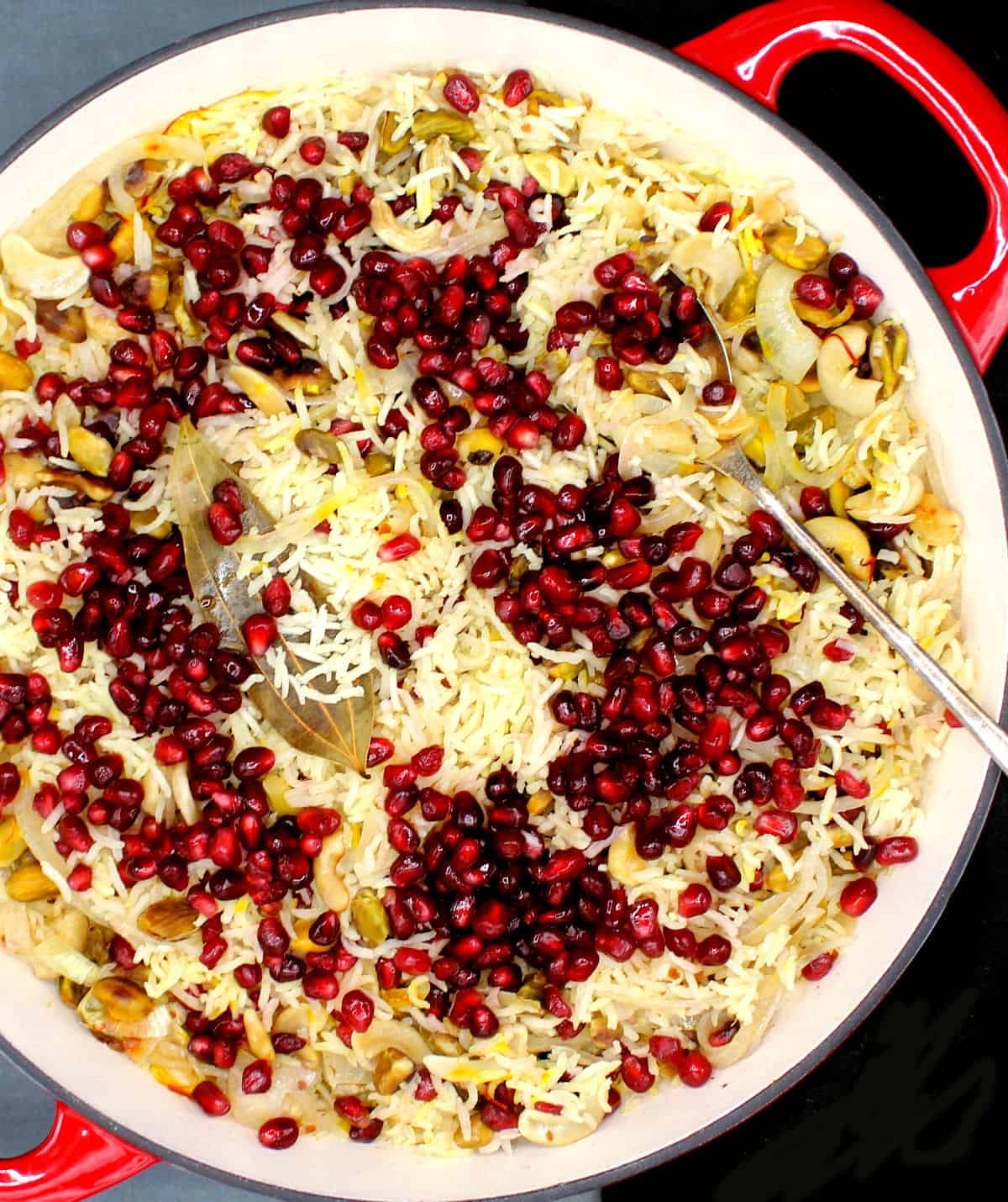 Overhead shot of a red skillet with pomegranate pilaf and a steel spoon.