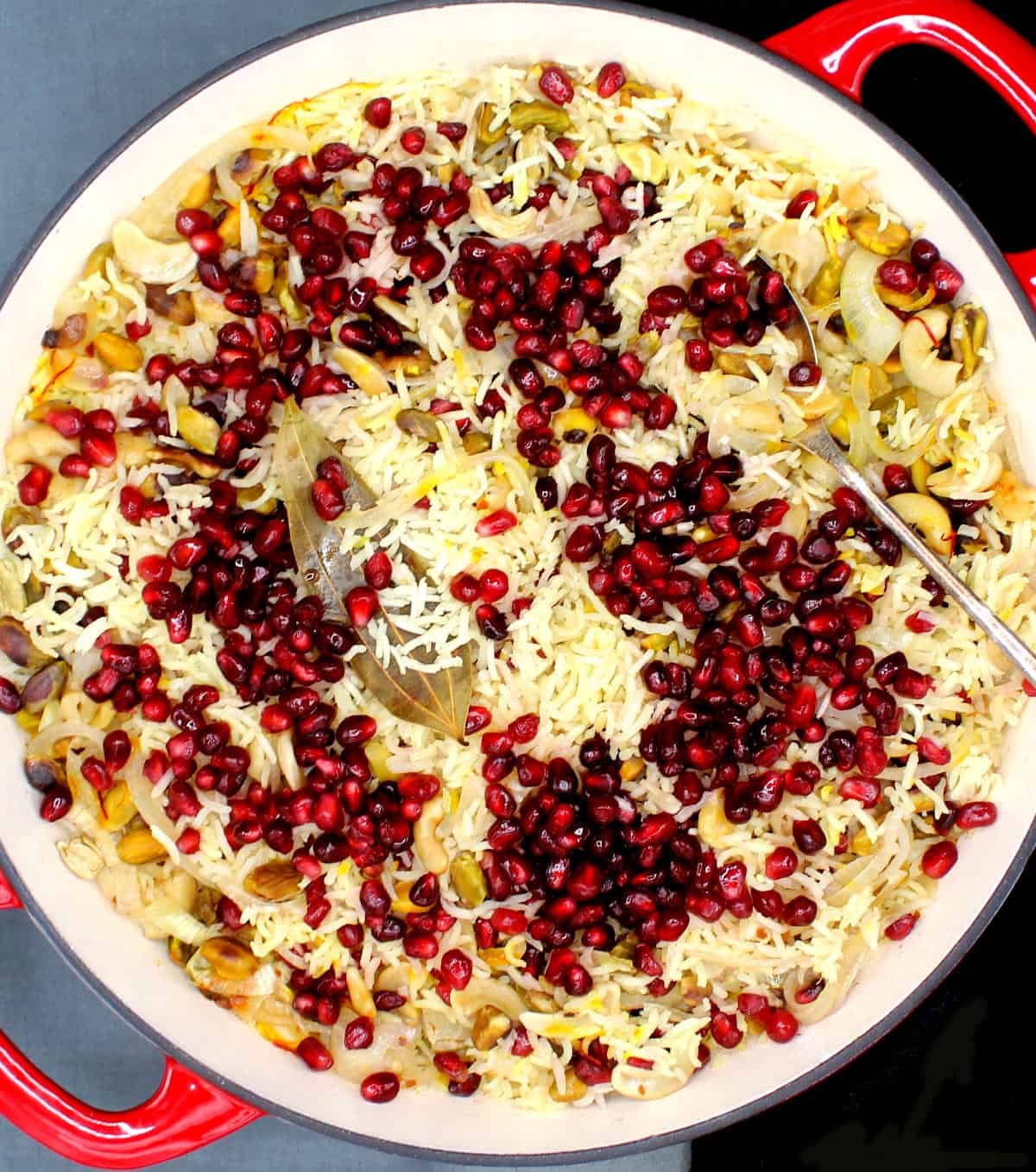 Overhead photo of a pomegranate pilaf in a red and white skillet with a spoon.