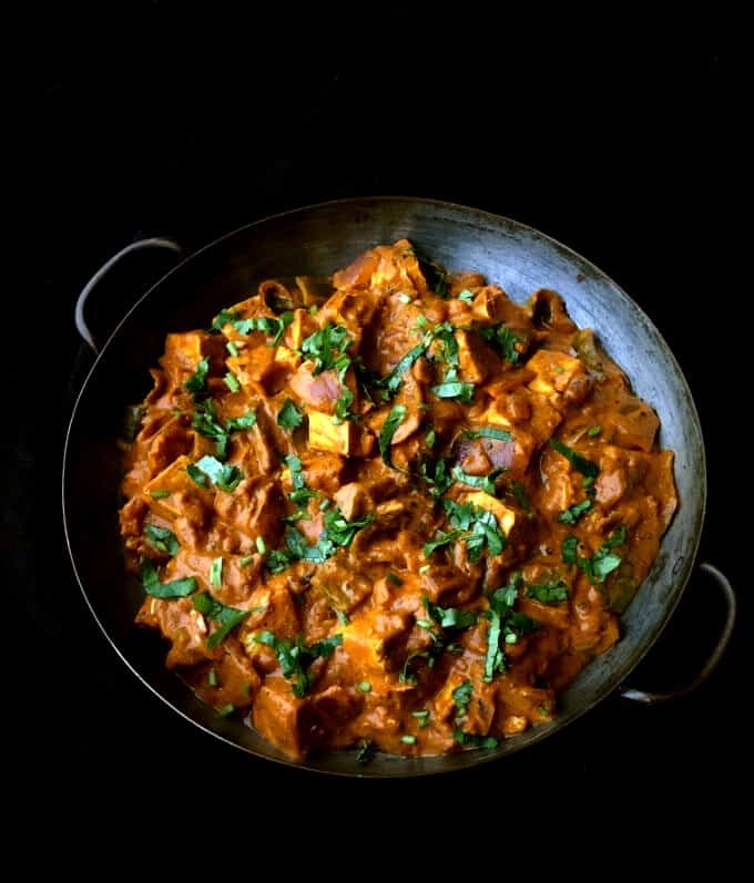 Front shot of a copper pan with tofu tikka masala with spiced tofu cubes in a tomato onion sauce and cilantro garnish.