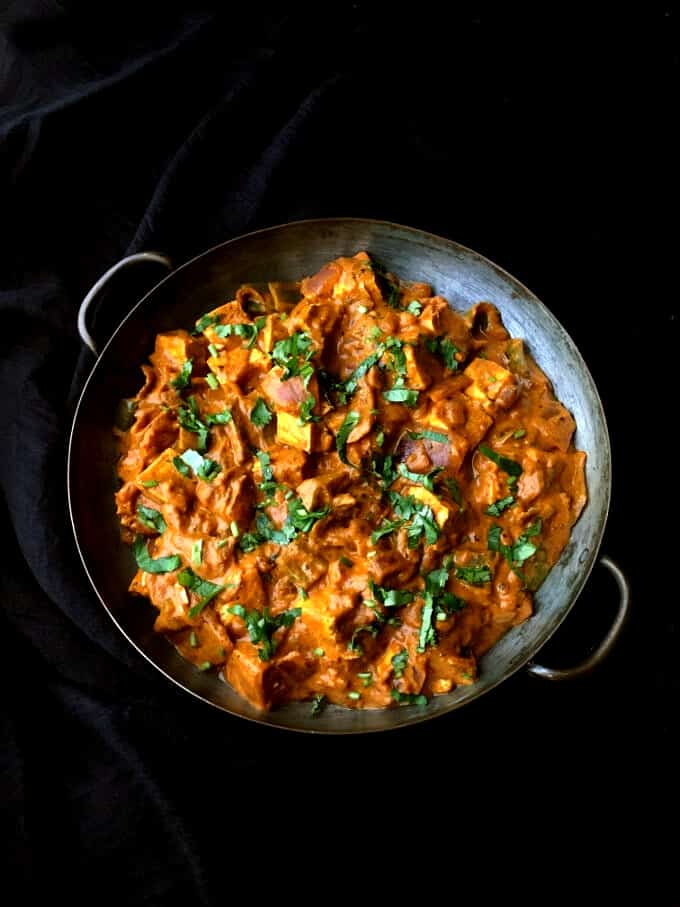 An overhead view of a copper pan with a delicious red tofu tikka masala with cilantro garnish on a black background.