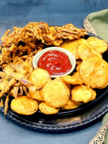 Front photo of a plate filled with veg pakoras and a red sauce with green napkin on the side.