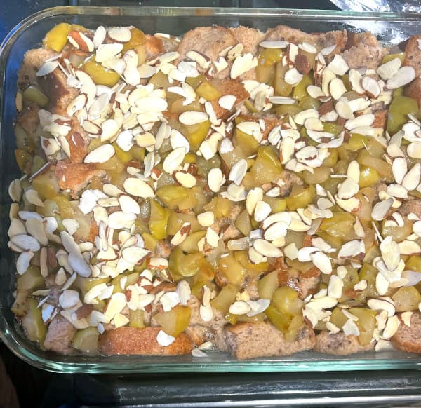 Pudding with almonds, apples and bread in custard assembled in baking dish.