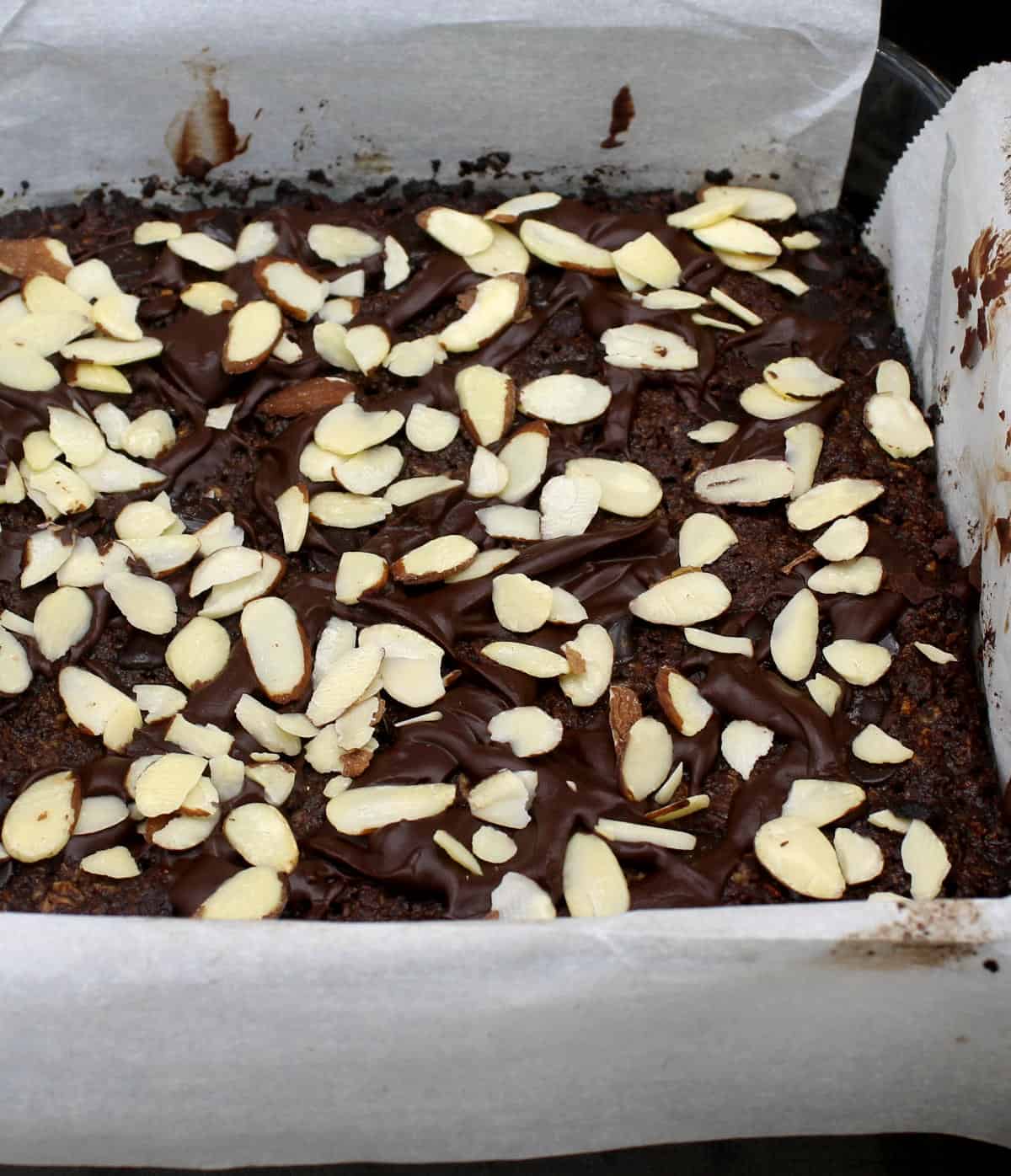 Front partial shot of vegan keto brownies with almond chocolate topping in glass baking pan lined with parchment.