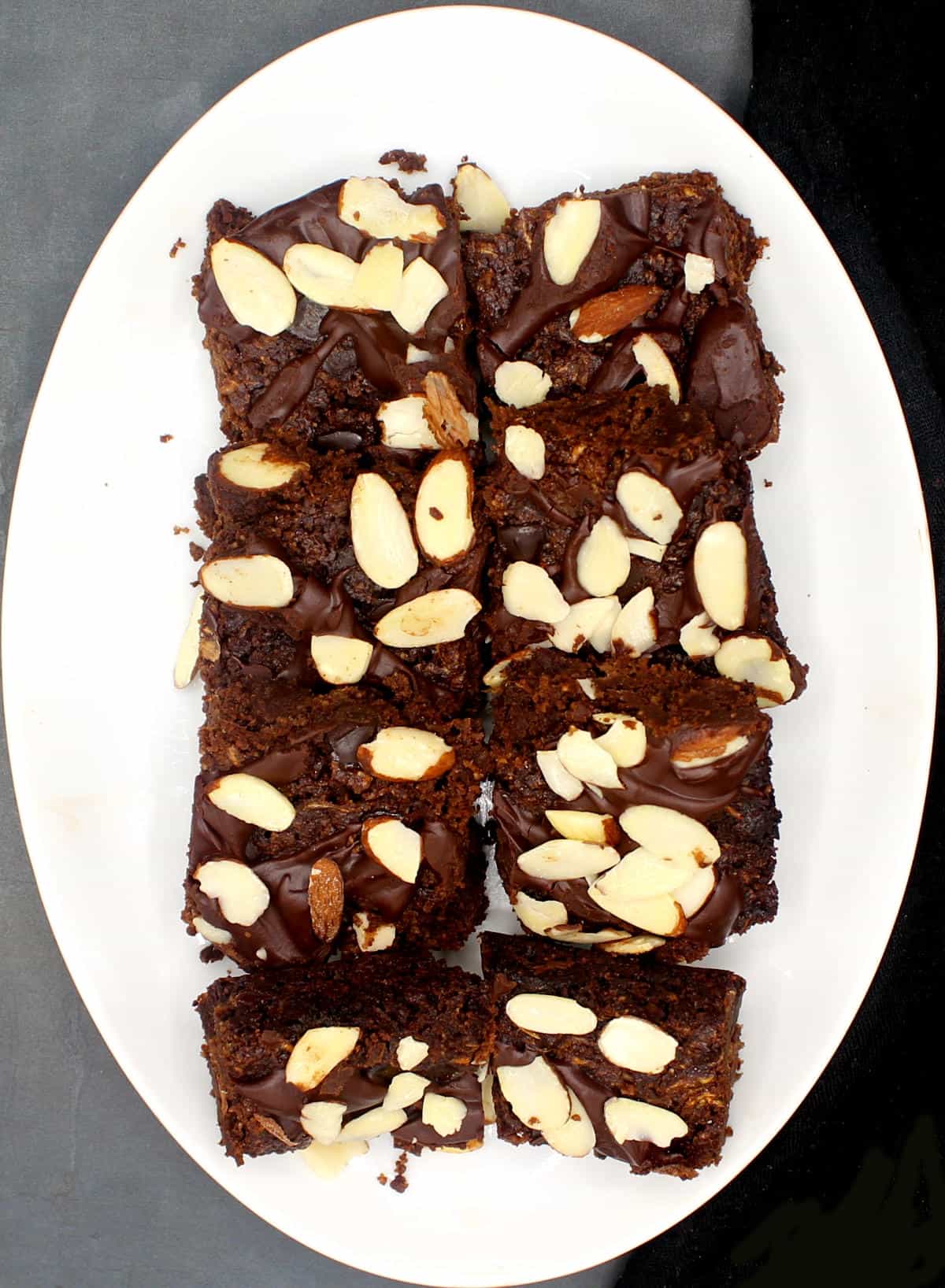 Overhead shot of squares of vegan keto brownies with almond and chocolate topping on a white oval plate.